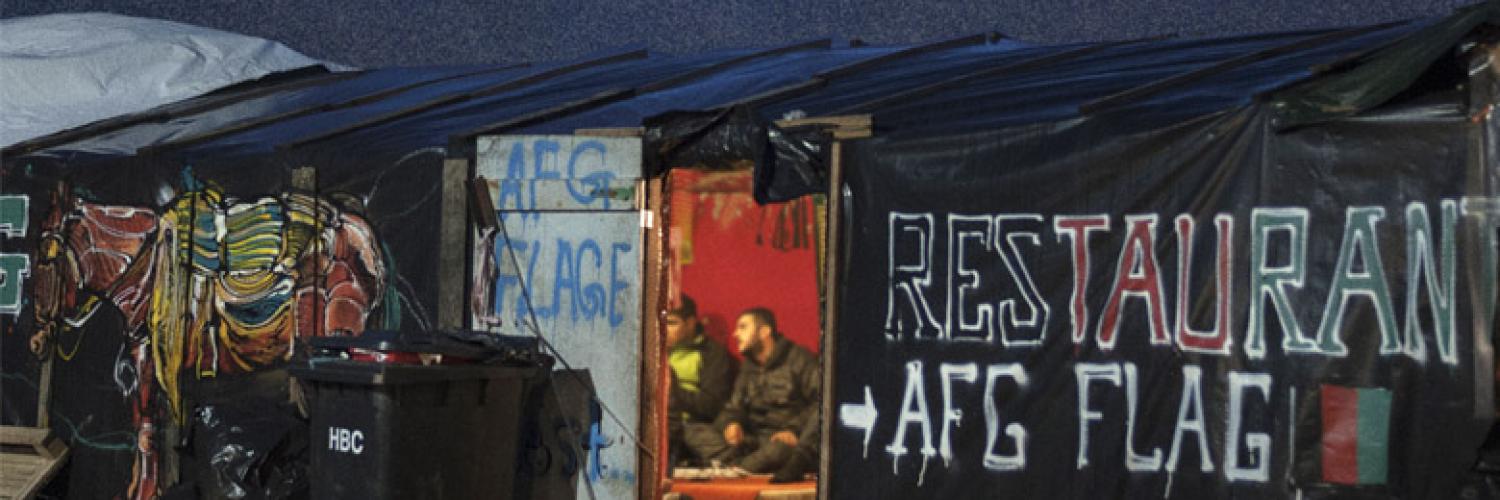 External photo looking into the dimly lit doorway of the temporary structure known as the Afghan Cafe in the Calais 'jungle' taken by  Giulio Piscitell