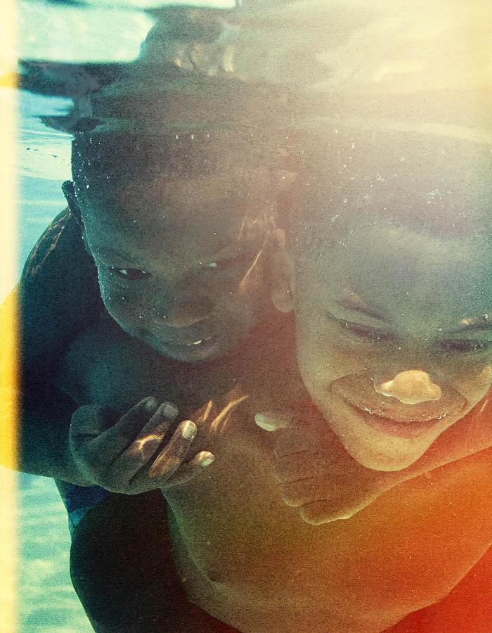 Two young boys under the water smiling, holding each other tightly