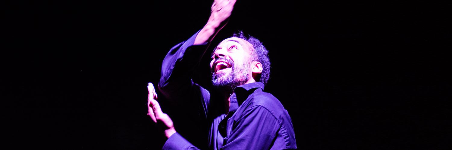 Man in a darkly lit atmosphere, arms stretched, looking upwards 