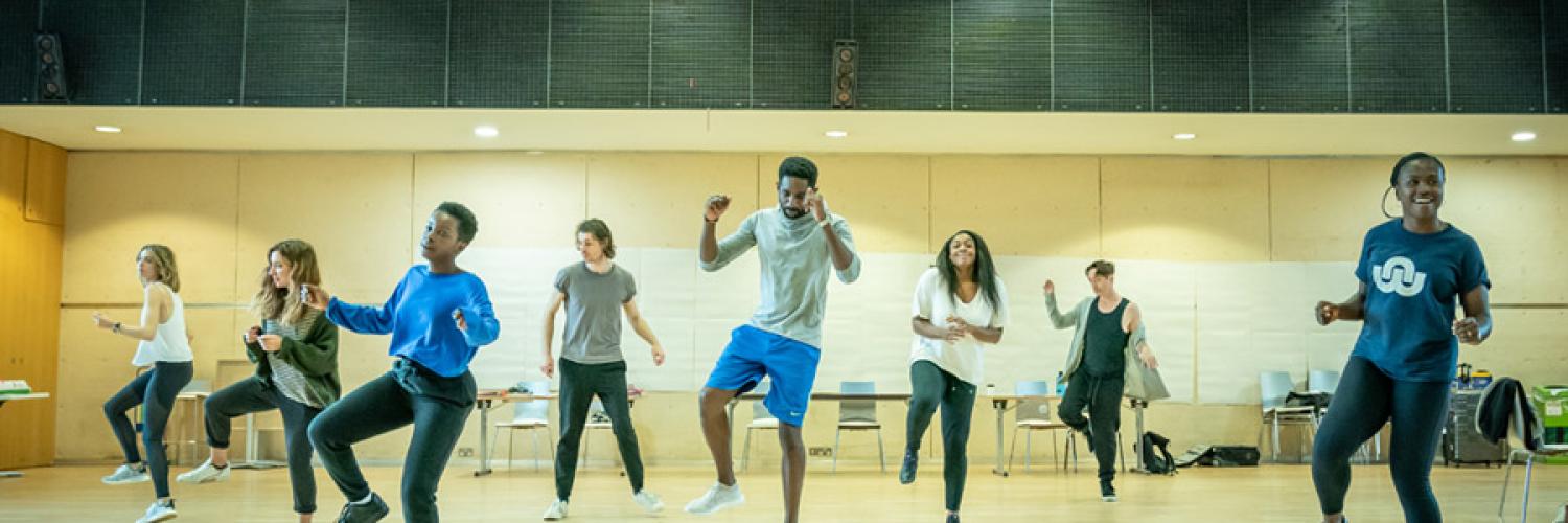 The company of Fairview dancing in a row in the rehearsal room