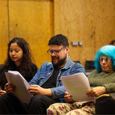 Three people sat on a sofa holding scripts. 