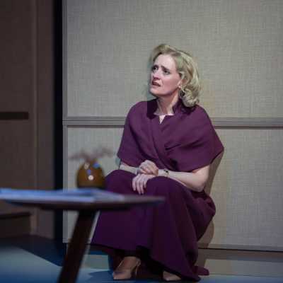 A female with blonde hair crouches against a wall. She is wearing a dark purple dress.