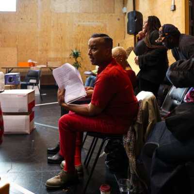 People standing and sitting with scripts in a studio with wooden walls