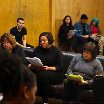 Three people sat on a sofa holding scripts. 