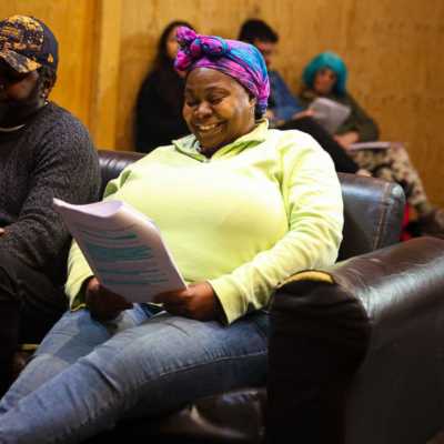 A person seated on a sofa smiling at a script they are holding. 