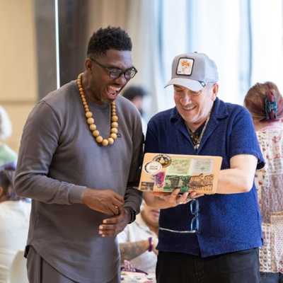 Kwame Kwei-Armah and Elvis Costello are stood close together looking at a laptop screen in Elvis's hands. They are laughing.