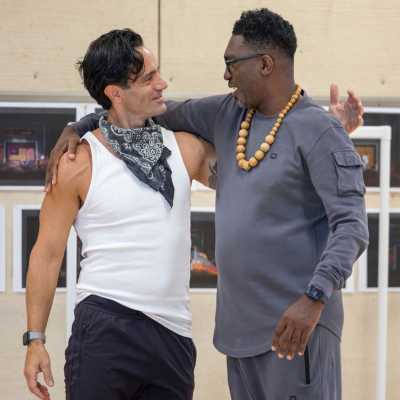 One of the shows leads and the director, Ramin Karimloo and Kwame Kwei-Armah, stand in front of photos of the set model. They have their arms around each others shoulders and are looking at each other