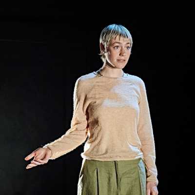 A person stands speaking with one arm out gesturing 