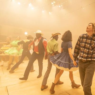 The cast of of Rodgers & Hammerstein's Oklahoma! all dancing in haze with golden light