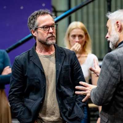 Four people stand, three forward facing and one with his back to the camera. Two are stood further back and out of focus. They look intently at the conversation happening between the two men in front of them. It looks like a serious conversation