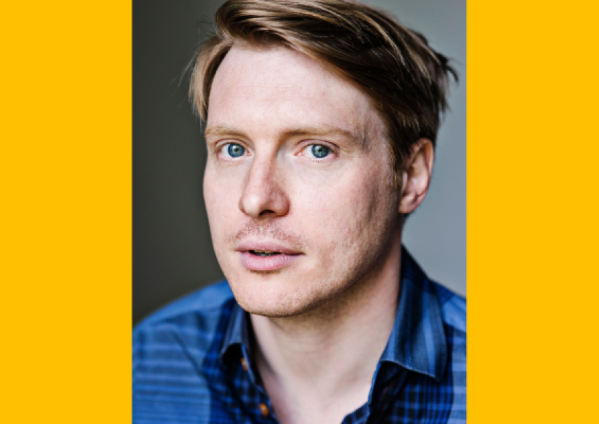 A headshot of a 5’11 Caucasian man with sandy hair and blue eyes wearing a blue collared shirt