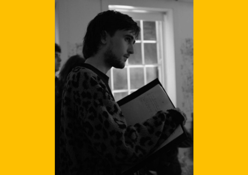 The side of a person wearing a jumper and holding a script. 