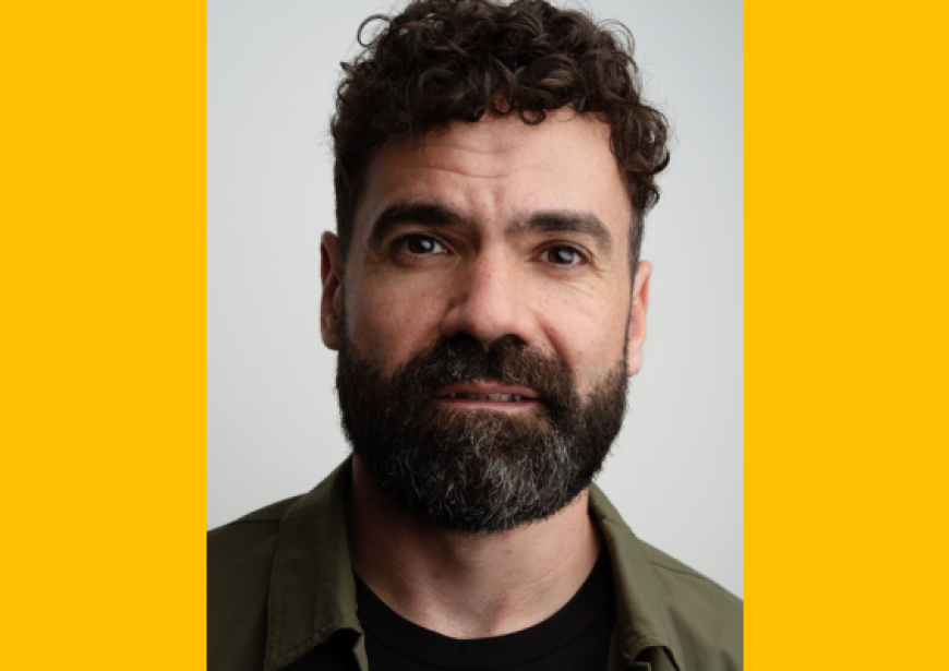 A headshot of a person with short dark hair as well as a beard and moustache.