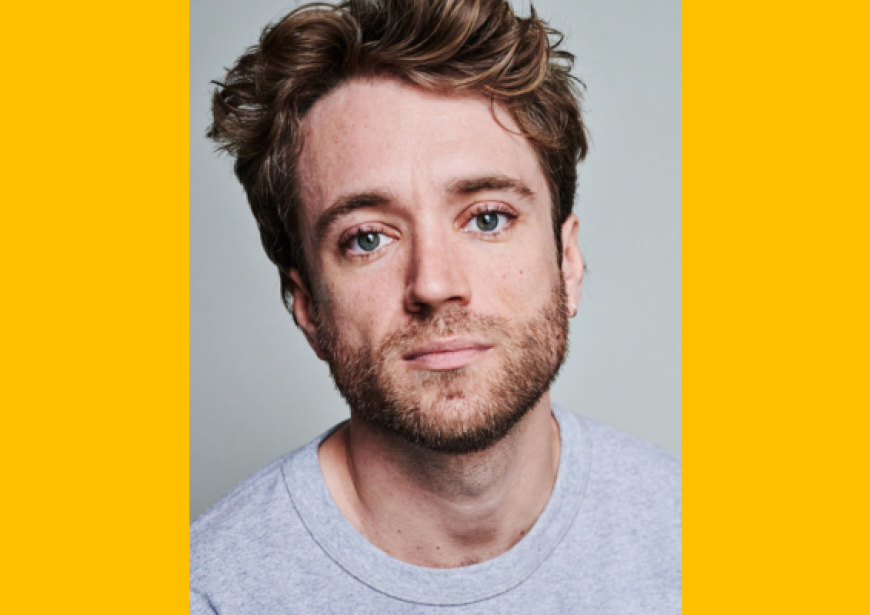 A headshot of a person with short brown hair and stubble