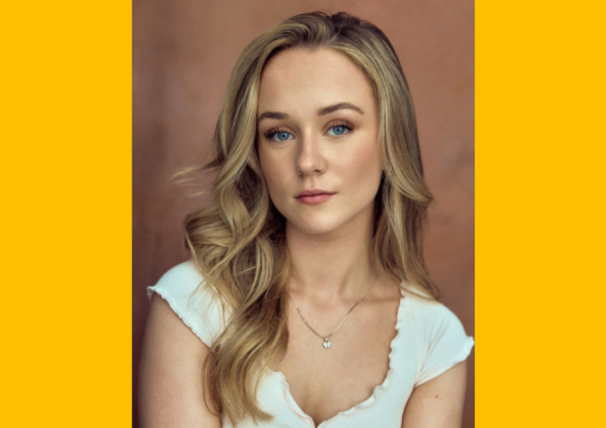 A headshot of a person with wavy blonde hair wearing a white top