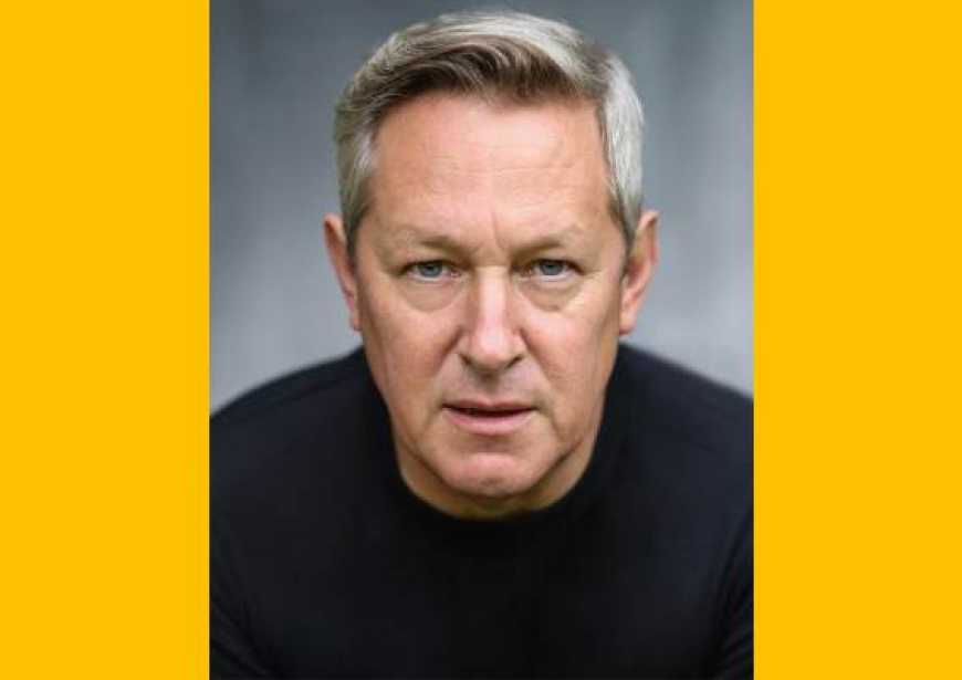 A headshot of a white man with cropped gray hair wearing a black top