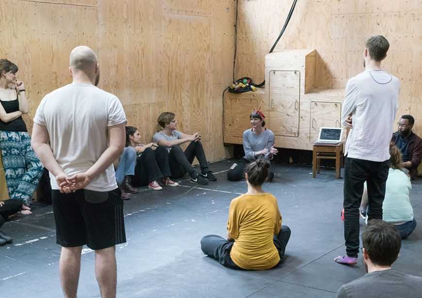 Kirsty Housely speaking to directors from the Genesis Network, facing her in a semi circle within a room of wood walls.