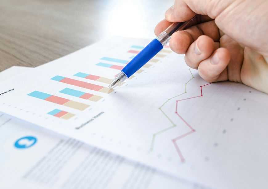 A close-up picture of a person's hand reviewing graphs and spreadsheets printed on paper