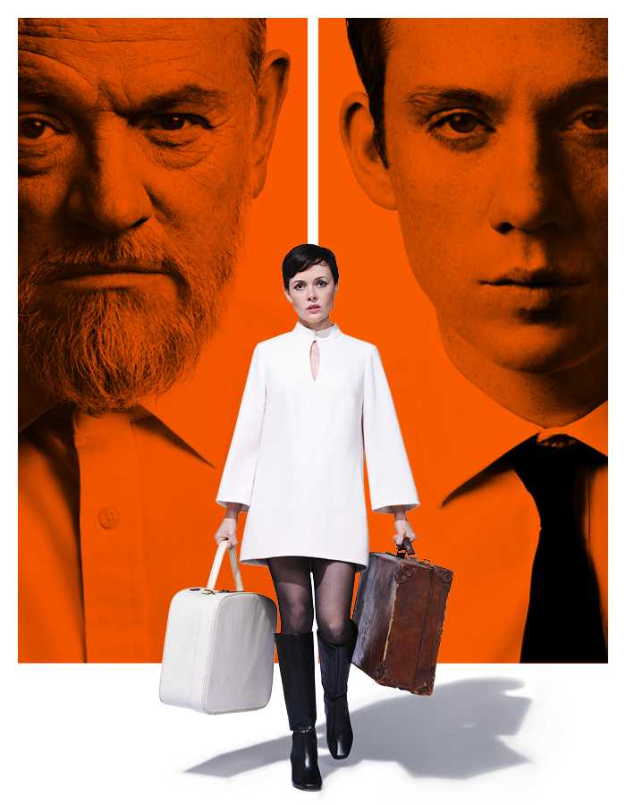 Two head and shoulder images of a man of Irish/Welsh heritage with a beard and a man with brown hair, blue eyes and freckles sit side by side in orange rectangles. Between them, a petite white woman with short dark hair wearing a white a-line dress and tall boots stands holding two suitcases. All three people are staring directly ahead. 