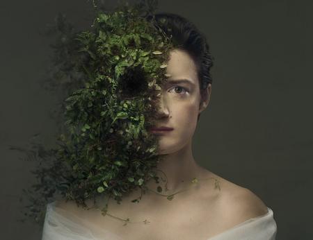 A sad looking bride played by Aoife Duffin looking straight at the camera.  She has a single teardrop about to fall from her right eye. The left side of her face is being overtaken with foliage. Photo by Sebastian Nevols. Concept by Emilie Chen. 
