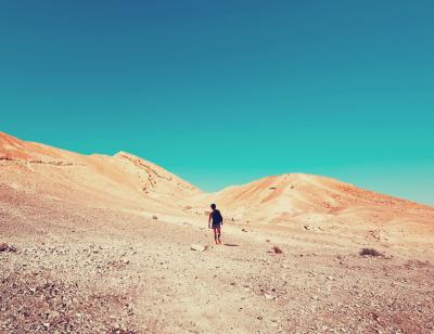 Boy walks through a desert towards two arid hills under a bright blue sky